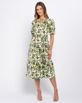 A woman modeling a short-sleeved midi dress with a green and white floral pattern, featuring puff sleeves and a keyhole neckline, set against a plain light gray studio background.