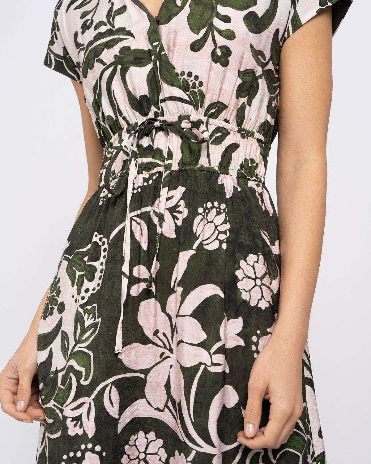 A close-up of a woman wearing a short-sleeve V-neck dress with a dark green, white, and pale pink floral print and a drawstring waist.