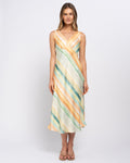 A woman modeling a sleeveless midi dress with a draped wrap-style bodice and diagonal striped pattern in pastel orange, teal green, and cream, set against a plain light gray studio background.