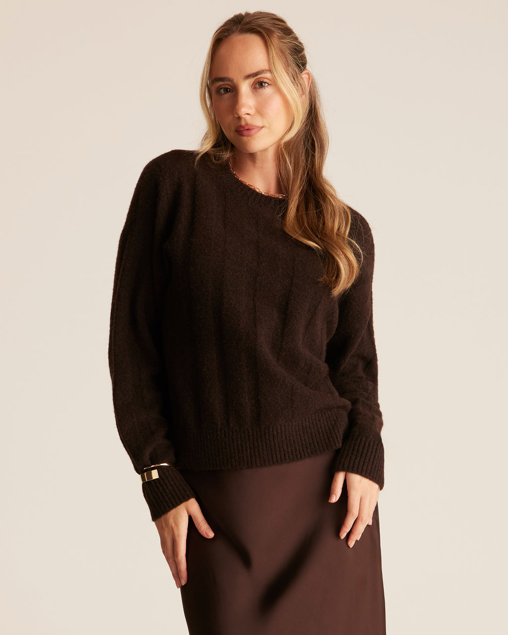 Woman wearing a brown sweater and skirt against a plain background