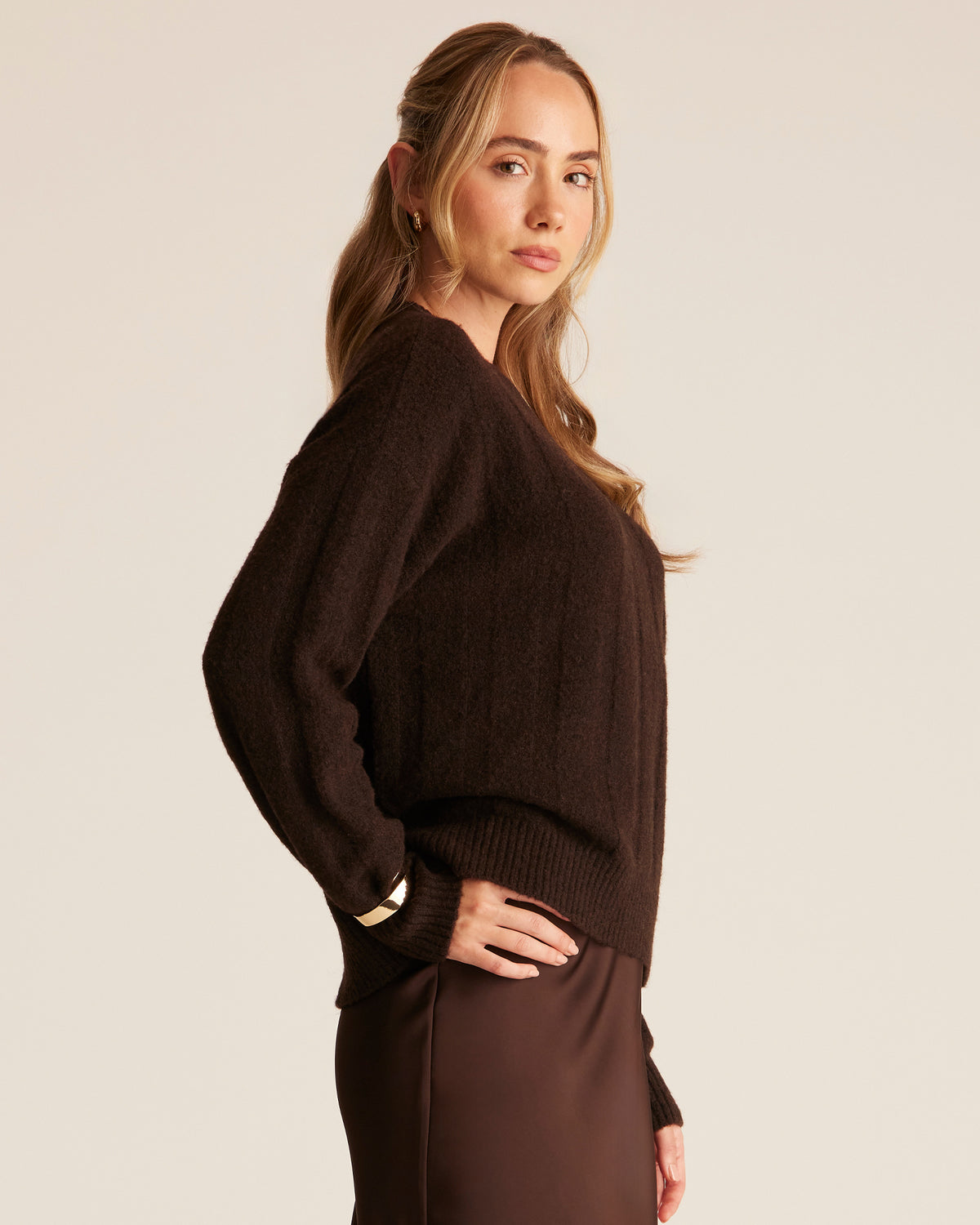 Woman wearing a brown sweater and pants against a beige background