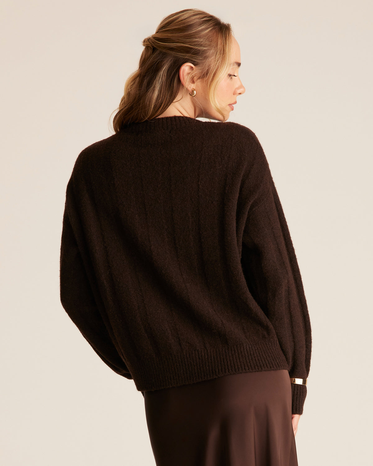 Woman wearing a brown sweater and skirt set against a plain background