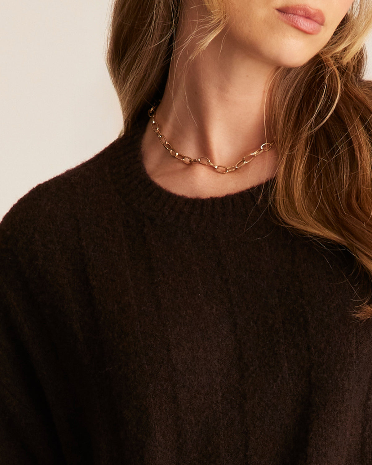 Person wearing a gold chain necklace with a plain background