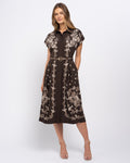 Stella Women's Angela Midi Dress - Mocha Garden. A woman models a dark brown midi shirt dress with beige floral embroidery, featuring a pointed collar, short sleeves, and a matching beige belt with a gold buckle.