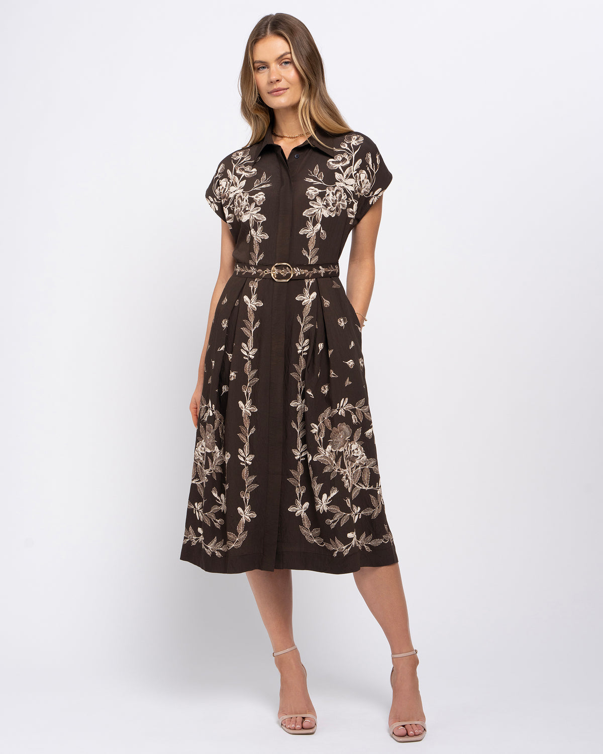 Stella Women's Angela Midi Dress - Mocha Garden. A woman models a dark brown midi shirt dress with beige floral embroidery, featuring a pointed collar, short sleeves, and a matching beige belt with a gold buckle.