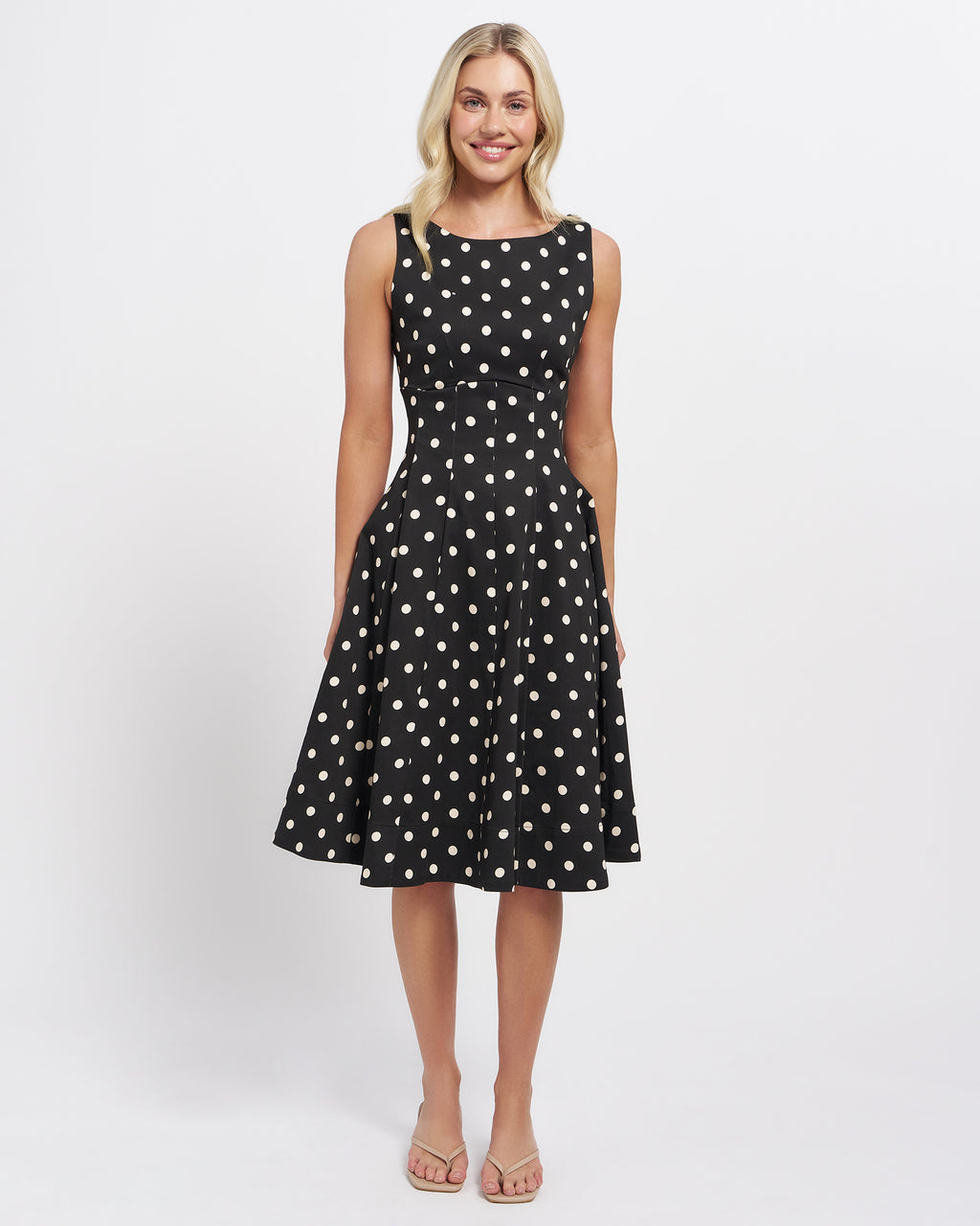 Stella Women's Molene Midi Dress - Black. A woman modeling a sleeveless black A-line dress with a cream polka dot pattern, standing against a plain white studio background.