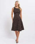 Stella Women's Molene Midi Dress - Chocolate. A woman modeling a sleeveless fit-and-flare dress with a brown base and white polka dots, standing against a plain light gray studio background.