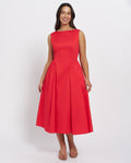 Stella Women's Tammy Midi Dress - Cherry. A woman modeling a sleeveless red midi dress with a boat neckline and a pleated skirt, standing against a plain light gray studio background.
