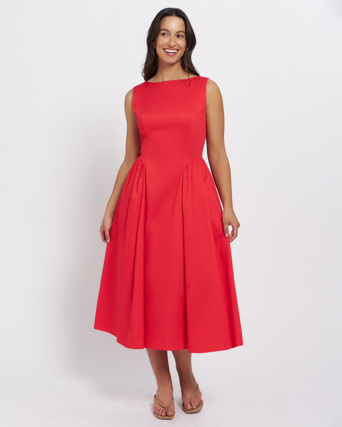 Stella Women's Tammy Midi Dress - Cherry. A woman modeling a sleeveless red midi dress with a boat neckline and a pleated skirt, standing against a plain light gray studio background.