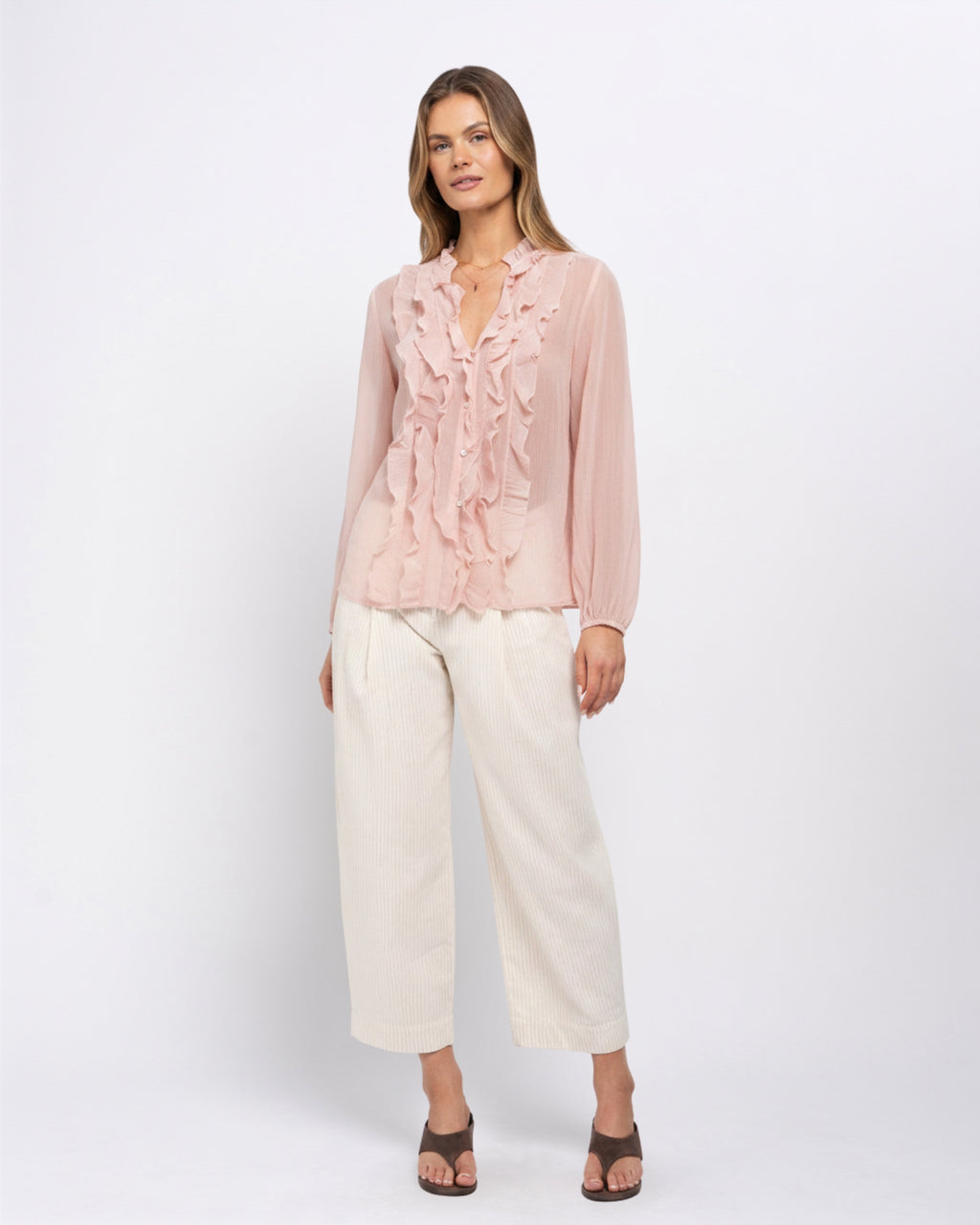 Woman modelling the Khloe Top in Ballerina pink, a ruffled V-neck blouse paired with cream wide-leg trousers