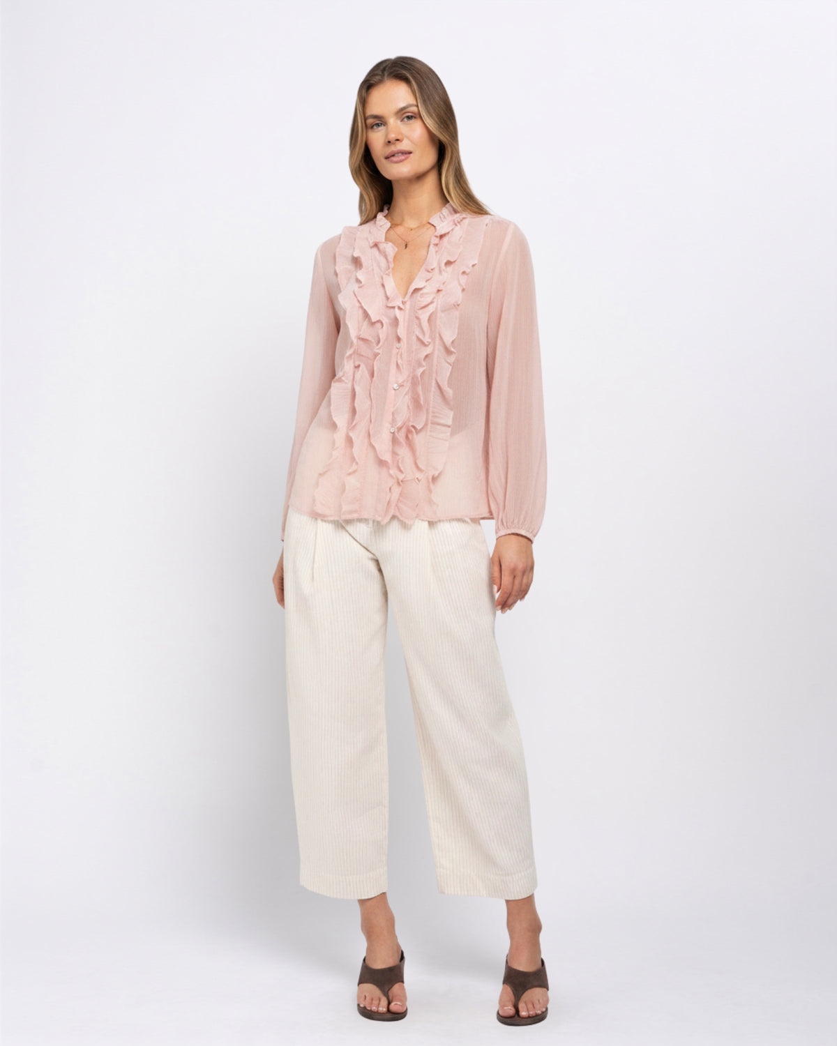 Woman modelling the Khloe Top in Ballerina pink, a ruffled V-neck blouse paired with cream wide-leg trousers